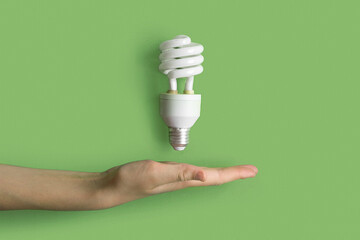 Compact fluorescent lamp Lamp in human hand. Helical integrated CFL Lightbulb on green pastel color...