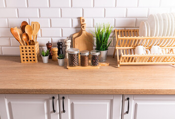 A set of stylish kitchen utensils plates, bowls, cutting boards, spoons on a wooden countertop opposite a white brick wall.