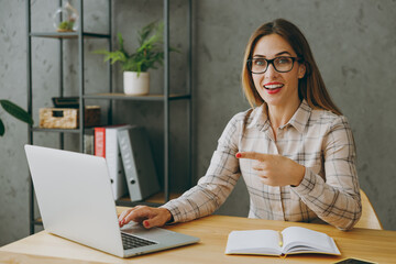 Young surprised shocked fun successful employee business woman wear shirt casual clothes glasses sit work at office desk with pc laptop, point index finger on computer. Achievement career job concept.