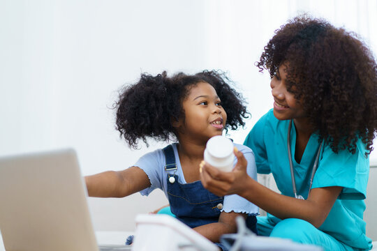 American - African Ethnicity Girl Sitting And Talking With Doctor And Doctor Explain About Treatment And Medicine To The Girl, A Professional Pediatrics Kindly Explains Or Talks With Little Girl.