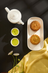 A set of tea decorated with two delicious mooncakes placed on a ceramic dish. Yellow fabric with flowers featured. Mid autumn festival chinese traditional ornaments