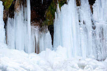 Frozen waterfalls on rocks with icicles in Iceland. Moss in ice. Spring warming, melting ice,...
