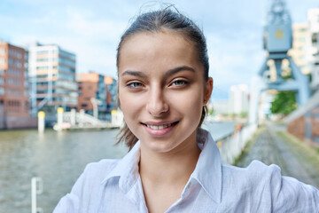 Headshot portrait of teenage girl looking at camera outdoors on city