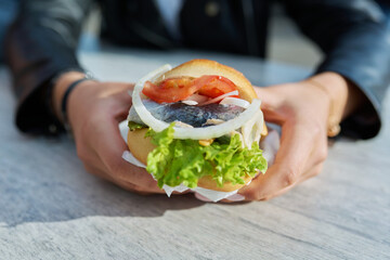 Traditional street sea food, burger with herring, close-up in outdoor hands