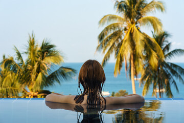 Young woman person in pool water on vacation relax and look on sea horizon and palms in tropical resort hotel. Rear view. Copy space