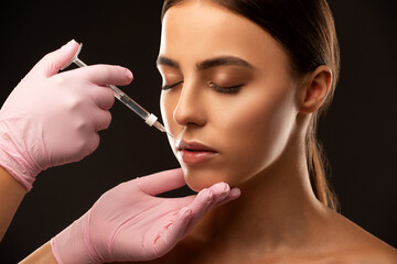 Fototapeta premium Cosmetologist does injections for lips augmentation and anti wrinkle in the nasolabial folds of a beautiful woman. Women's cosmetology in the beauty salon.