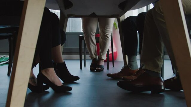 Close-up of legs of multiracial group of business people sitting at table during meeting in office