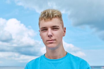 Headshot portrait of handsome smiling teenage guy, blue sky