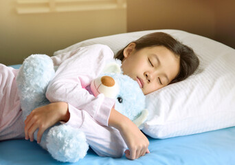 Adorable little Asian girl with black hair sleeping in the bed with her toy. The child girl hugs...