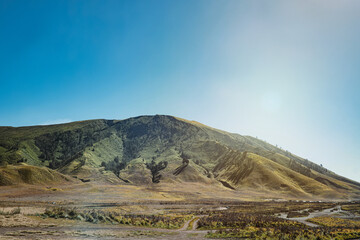 Bukit Teletubbies or Teletubbies Hill located behind Mount Bromo with clear blue sky