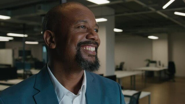 Portrait of happy mature black man in businesswear looking away by desk in office