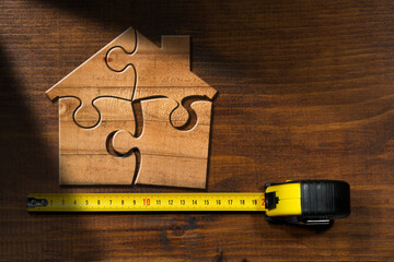 Wooden jigsaw puzzle pieces forming a house shape, on a wooden workbench with yellow and black tape...