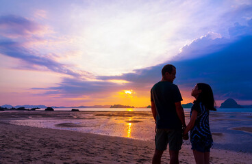 Silhouette Asian father and teenage daughter holding hands talking, standing together on sunset...