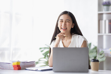 Happy young Asian girl working at a office with a laptop calculator to calculate business accounting statistics concept