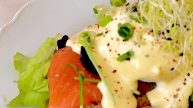 Eggs benedict with salmon and avocado on a slice of wholewheat bread for breakfast or brunch in a restaurant, slow motion