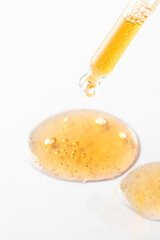 Dropper pipette with drops of yellow liguid on white background .Cosmetic product, science and research