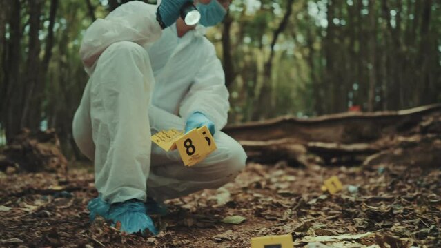 Man forensic police investigator putting numbered markers of evidences on a crime scene