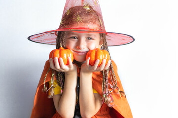 happy little girl with pigtails dreadlocks with pumpkin in witch costume, hat, laughing, smiling, scaring and saying boo. Child for fun scary halloween holiday
