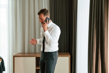 Business call, talking by phone. Man is indoors in the hotel room