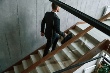 Walking up. Man in business suit and tie with case in hands is on the stairs