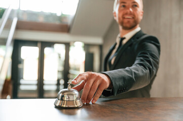 Standing, using hotel desk bell. A man in a black jacket at the hotel reception