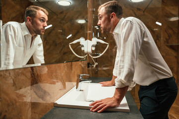Man in formal clothes is in the bathroom against mirror