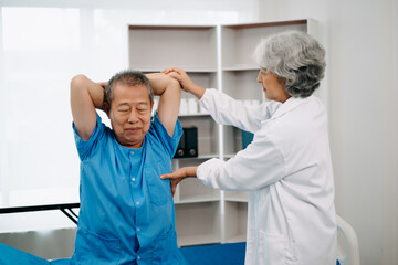 Obraz premium Asian physiotherapist helping elderly man patient stretching arm during exercise correct with dumbbell in hand during training hand in bed in clinic