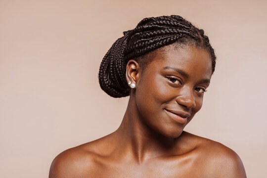 Beauty portrait of african girl with clean healthy skin over beige background. Smiling female with black braided hair, top knot hairstyle.