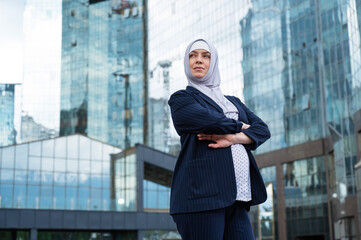 Portrait of a pregnant business woman in a hijab and a suit with crossed arms on her chest outdoors.