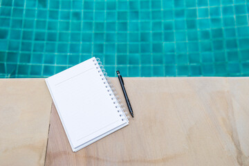 Blank note book on swimming pool edge with space on blurred swimming pool background, outdoor day light, education concept