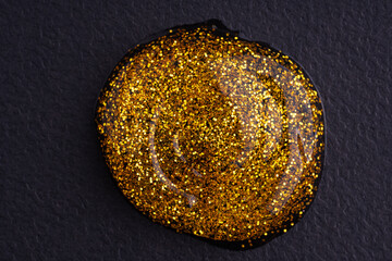 Round swatches of golden glitter paint on black paper background.