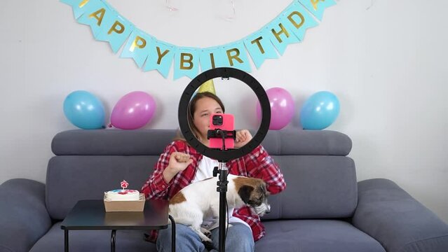 teenage girl with her funny pet dog are celebrating her birthday and are filming a video for their Tiktok vlog at their home. Gen Z talent play video selfie shoot app for show share viral story. 