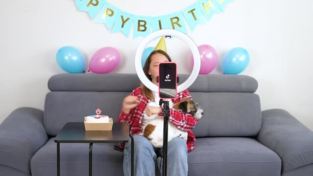 Teenage girl with her funny pet dog  are filming a video for their Tiktok vlog at their home. Tiktok logo. Gen Z talent play video selfie shoot app for show share viral story. 