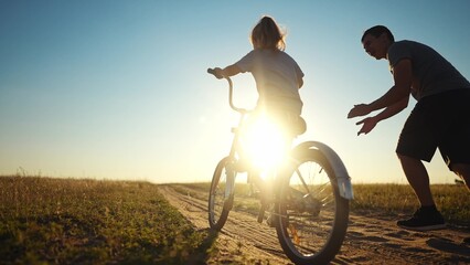 dad teaches daughter to ride a bike. happy family childhood dream concept. father and little...