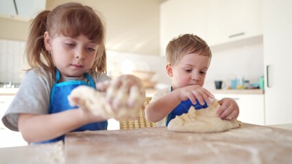 children making dough in the kitchen. baby boy cook in the kitchen knead dough and flour indoors. happy family kid lifestyle dream concept. children play cooking dough together at home