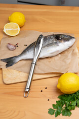 Fresh dorado fish with fish scales and fish cleaner for removing fish scales on the kitchen wooden table. Devices for the kitchen.