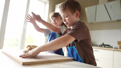 Fototapeta premium children kids making dough in the kitchen. baby boy cook in the kitchen knead dough and flour lifestyle indoors. happy family kid dream concept. bake children play cooking dough together at home