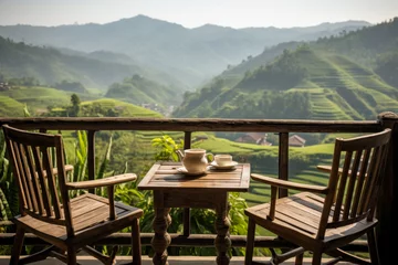 Poster wooden terrace with wooden chairs coffee mugs on the table landscape view of terraced rice fields and mountains is the background in morning warm light © Attasit