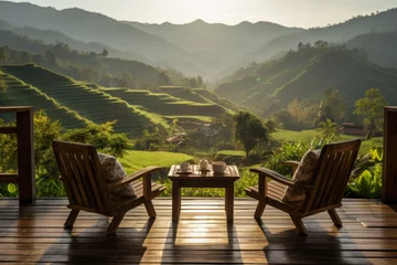 Fototapeten wooden terrace with wooden chairs coffee mugs on the table landscape view of terraced rice fields and mountains is the background in morning warm light © Attasit