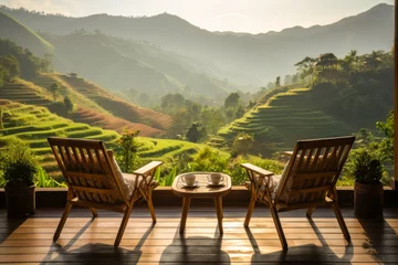 Fototapeten wooden terrace with wooden chairs coffee mugs on the table landscape view of terraced rice fields and mountains is the background in morning warm light © Attasit