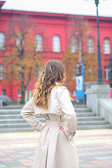 A girl in a beige raincoat against the background of Taras Shevchenko University. Red facade. Historical part of Kyiv. Europe. Tourism concept