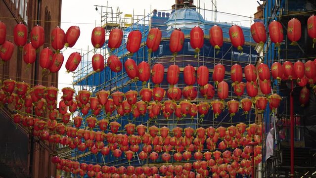 plenty of red lanterns hanged in China town in the middle of the street above windy weather moving flying around construction with blue material wrapped around repairing building in the background
