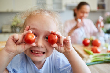 Cute blond girl holding ripe cherry tomatoes at home