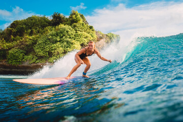 Attractive surf girl riding on surfboard in ocean. Surfer on blue wave during surfing
