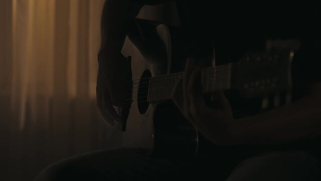 Closeup shot of a man sitting in the living room, playing song on the acoustic guitar using guitar pick. Everyday life creative concept.