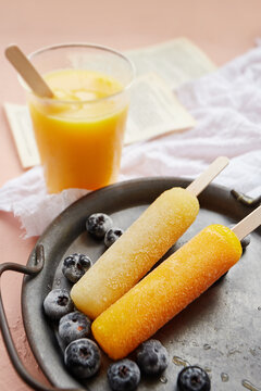 Close-up of an ice lolly in a glass of orange juice with frozen blueberries