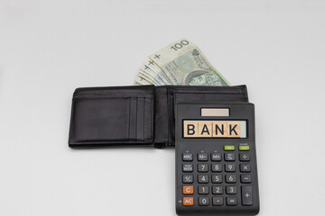 Wallets with banknotes of 100 zloty denominations next to which lies a wooden Bank sign on a calculator. The concept of spending during a crisis of inflation and recession. 