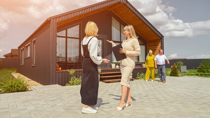 Blonde realtor talking to woman ready to buy summer house for elderly parents. Potential customer listens to real estate agent introducing offered cottage, sunlight