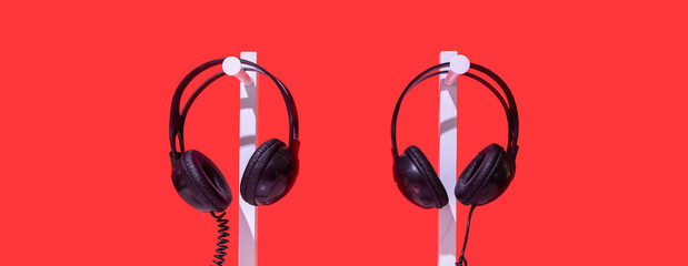 Two pairs of black headphones on stand. Red background, white table and black noise reduction...