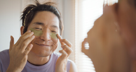 Gay queer man non-binary beauty blogger makeup artist at home cross dressing up apply face skin care eye make up brush. Real asia LGBT young guy adult people happy relax smile looking at mirror pride.